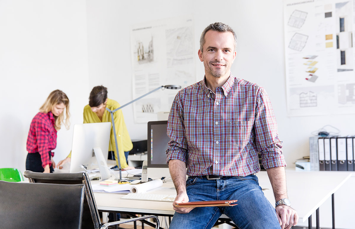 Mitarbeiter im Büro für nachhaltiges Bauen vor laufender Projektarbeit im Hintergrund